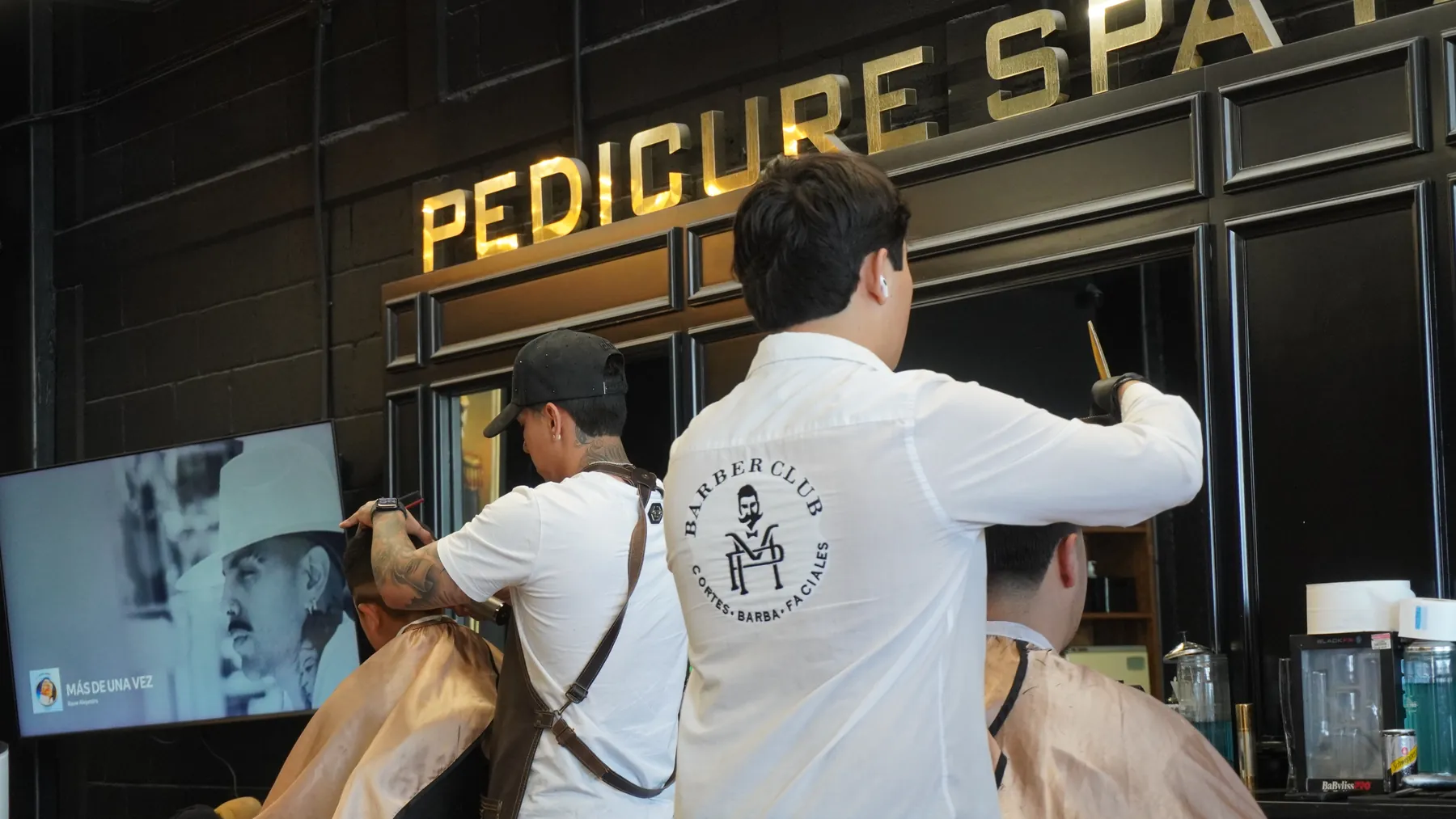 Barberos trabajando bajo el letrero Pedicure Spa de MP Barber Club